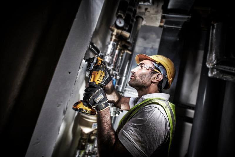 Arbeiter nutzt einen DEWALT DCS355D2 an einer Wand, trägt Schutzkleidung und Handschuhe.