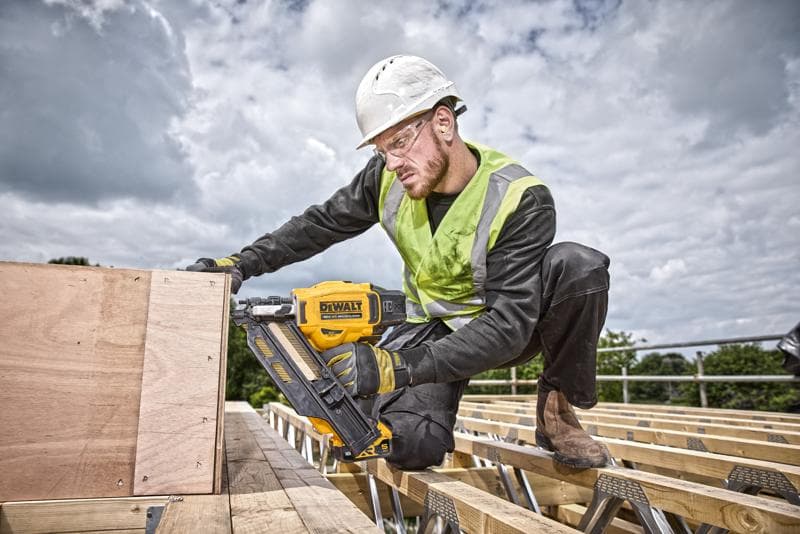 Person nutzt DEWALT Nagelpistole DCN930N auf Holzbrettern, im Freien auf Baustelle, trägt Sicherheitsausrüstung.