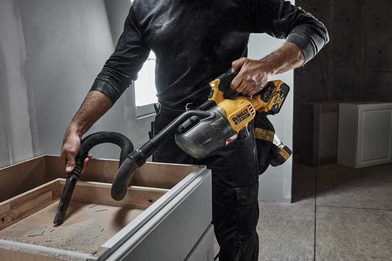 Person reinigt einen Holzschrank mit einem kabellosen DEWALT Handstaubsauger während Renovierungsarbeiten.