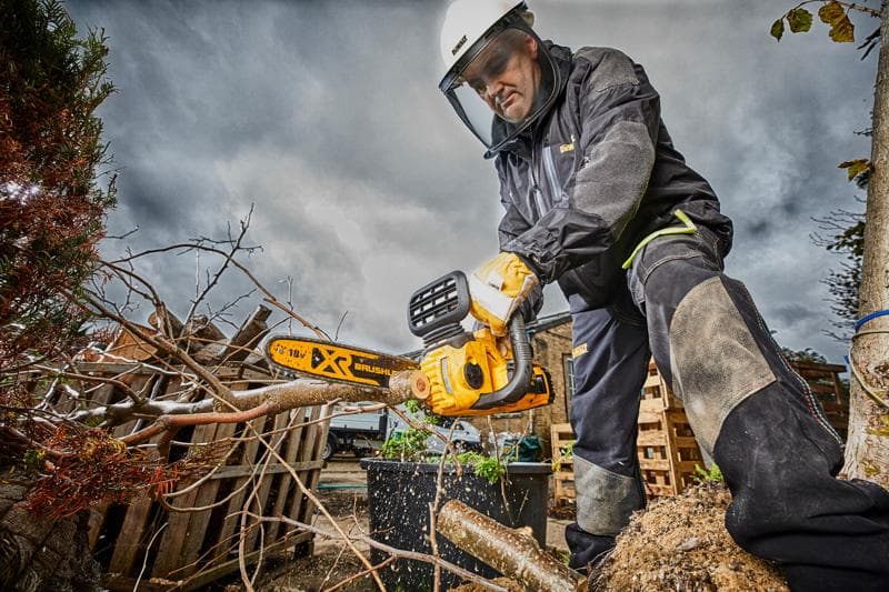 Person mit Schutzkleidung nutzt eine DEWALT Kettensäge und schneidet Äste draußen an einem wolkigen Tag.