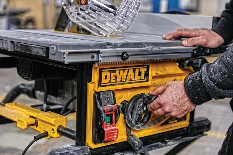Nahaufnahme einer Person, die die Einstellungen einer DEWALT Tischkreissäge anpasst, mit gelbem Bedienfeld mit Schaltern und Drehknöpfen in einer Werkstatt.