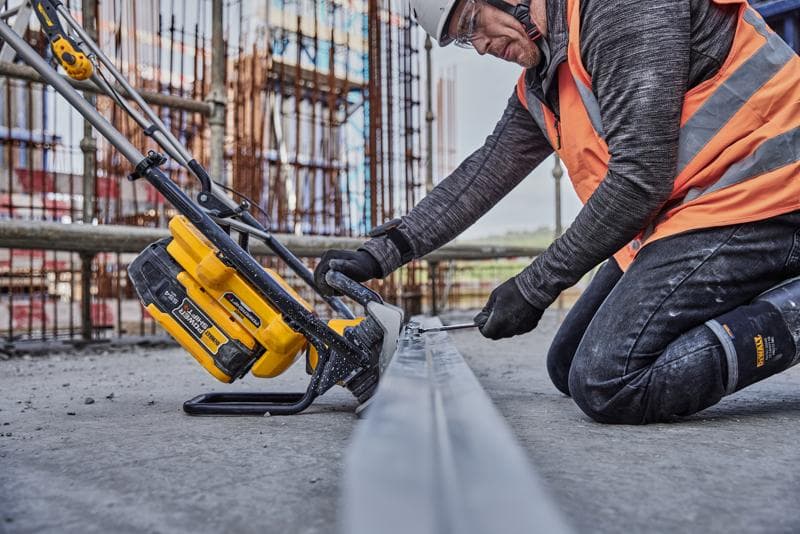 Arbeiter sägt Metall mit gelbem DEWALT Werkzeug auf Baustelle, trägt Sicherheitskleidung und orange Weste.