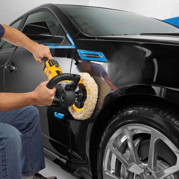 Person poliert den Kotflügel eines schwarzen Autos mit DEWALT Polierer in der Garage.