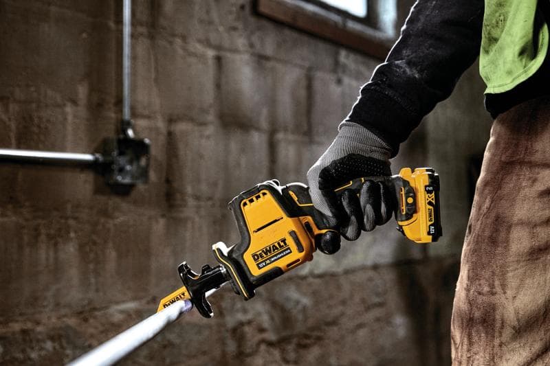 Hand mit Handschuh hält DEWALT DCS312D2 Akku-Säbelsäge und schneidet ein Metallrohr drinnen.