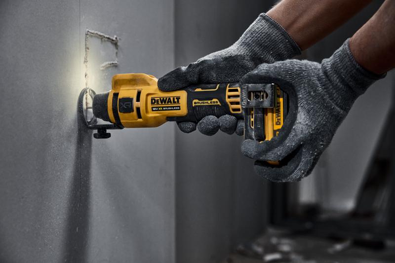 DEWALT kabelloses Drehwerkzeug schneidet Gipskarton, bedient von behandschuhter Hand.