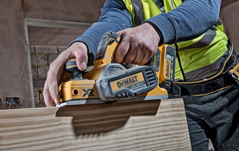 Person verwendet einen DEWALT DCP580N Akkuhobel auf Holz an einer Baustelle.