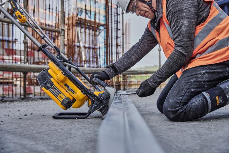 Arbeiter sägt Metall mit gelbem DEWALT Werkzeug auf Baustelle, trägt Sicherheitskleidung und orange Weste.